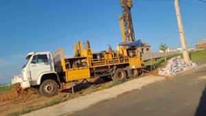 Caminhão de perfuração amarelo equipado para instalação de poços artesianos em terreno urbano.