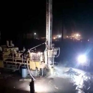 Equipamento de perfuração de poços em operação noturna com iluminação intensa.
