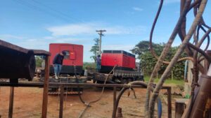 Geradores industriais vermelhos em um local de perfuração de poço artesiano com um trabalhador verificando o equipamento.